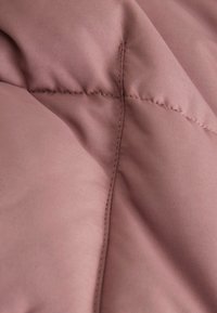 Mjukt, mauve sammanflätat tyg med subtil lyster, synliga sömmar och en slät yta som framhäver en puffig och strukturerad design.