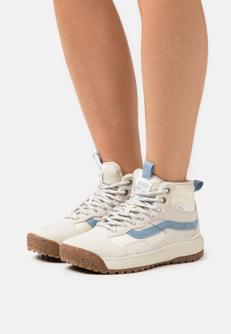 Høye sneakers laget av beige kanvas med lyseblå detaljer, med riller i gummisålen og metalløyler; snørt med flate, lysegrå snorer.