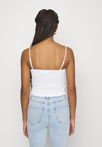 Débardeur blanc à smocks avec des fines bretelles, associé à un jean taille haute bleu clair avec poches arrière et coupe ajustée.