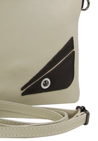 Crossbodytas van crèmekleurig synthetisch materiaal, met een contrasterend donkerbruin driehoekig accent, een zilverkleurige ronde drukknoop en verstelbare riem.