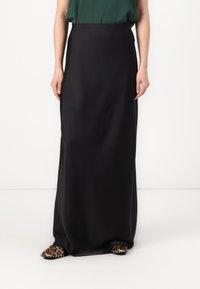 Schwarzer, knöchellanger Rock aus glattem Stoff mit hoher Taille. Kombiniert mit flachen Schuhen im Leopardenmuster. Schlichte, elegante Silhouette.