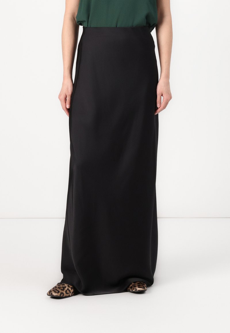 Schwarzer, knöchellanger Rock aus glattem Stoff mit hoher Taille. Kombiniert mit flachen Schuhen im Leopardenmuster. Schlichte, elegante Silhouette.