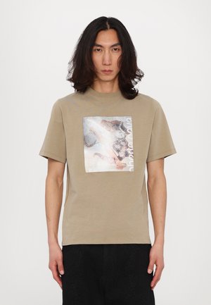 Beige katoenen T-shirt met een vierkante, metallic grafische print met een gemengd ontwerp. Korte mouwen en een ronde hals, ontspannen pasvorm.