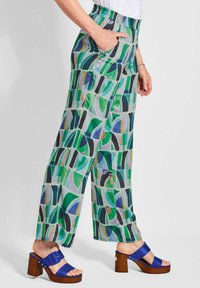 Lichte, geprinte wijde broek met geometrische ontwerpen in groen, blauw en zwart. Elastische tailleband en zijzakken. Gecombineerd met blauwe hakkensandalen.