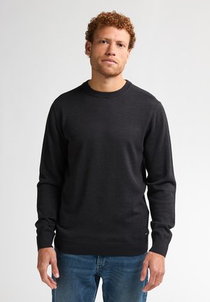 Suéter gris oscuro con cuello redondo, cuello y puños acanalados, hecho de una tela suave. Lleva puesto con jeans azules, sin patrones visibles.