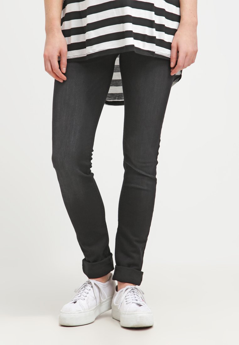 Calças skinny pretas com uma textura suave, combinadas com uma blusa listrada em preto e branco e ténis brancos. As calças têm as bainhas dobradas.