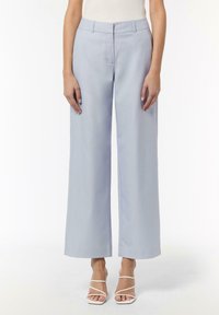 Helle blaue Hose im weiten Schnitt mit glatter Textur, ausgestattet mit einem taillierten Bund und vorderen Falten. Getragen mit weißen Riemchensandalen.