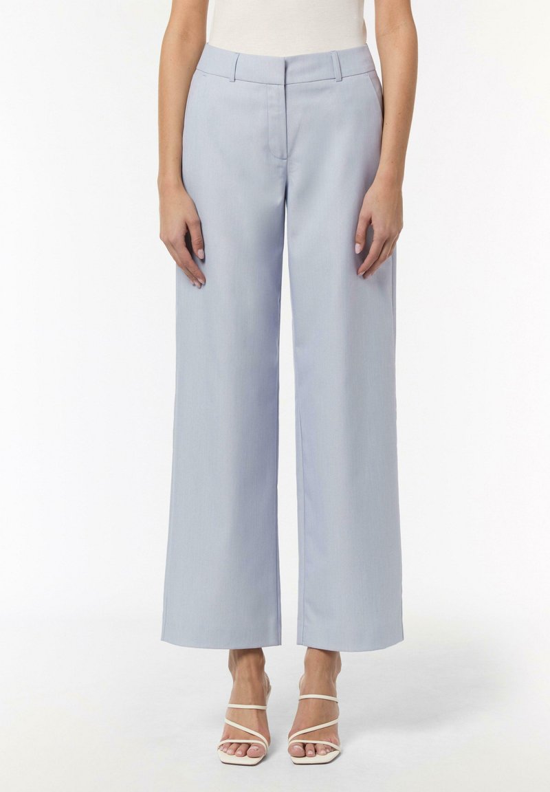 Helle blaue Hose im weiten Schnitt mit glatter Textur, ausgestattet mit einem taillierten Bund und vorderen Falten. Getragen mit weißen Riemchensandalen.