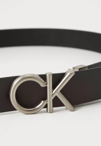 Black leather belt featuring a round silver-tone "CK" logo buckle, with a sleek, smooth texture and minimal design.