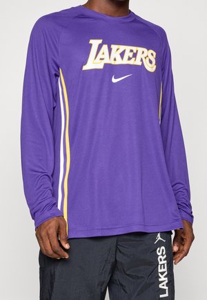 Homme portant un t-shirt à manches longues violet des Lakers avec des bandes jaunes et blanches et un pantalon noir avec un marquage blanc des Lakers et un logo Jumpman.