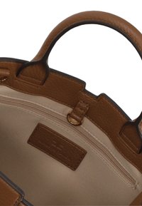 Interno di una borsa a tracolla in pelle marrone con rivestimento beige liscio. Le caratteristiche includono una tasca con zip e un'etichetta del marchio cucita all'interno. Manici arrotondati.