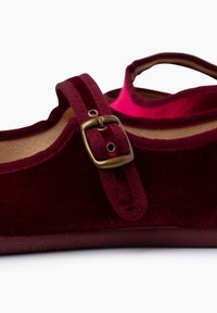 Chaussure plate en velours bordeaux avec un bout rond, un dessus texturé et une sangle décorative avec un détail en boucle en laiton.