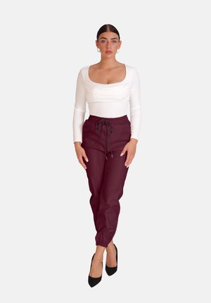 Weißes Langarmoberteil mit Rundhalsausschnitt, kombiniert mit bordeauxroten Hose mit elastischem Bund, die Bündchen und Taschen hat, getragen mit schwarzen High Heels.