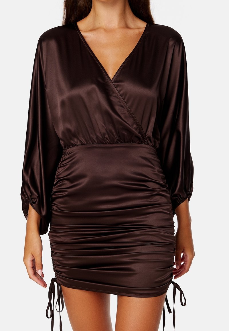 Brun satin klänning med djup V-ringning, elastisk midja och rynkade sidor. Långärmade med elastiska manschetter och justerbara snören vid fållen.