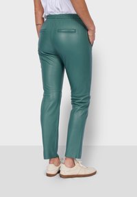 Pantalones de piel en color azul verdoso con cinturilla elástica, corte slim, bolsillos traseros y dobladillo a la altura del tobillo, combinados con zapatillas blancas.
