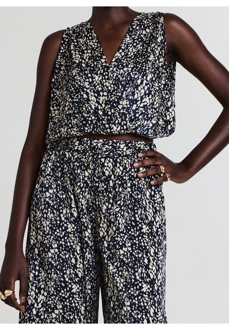 Crop top sans manches bleu marine et blanc à motif abstrait et pantalon large taille haute assorti porté par une personne avec des bagues aux deux mains.