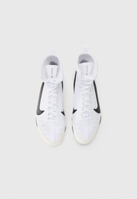 White high-top sneakers with a textured surface, black accents, and white laces. Features a rounded toe and a padded ankle collar.