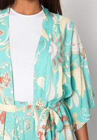 Turkusowe kimono z kwiatowymi i paisley wzorami, krótkimi rękawami i paskiem w talii. Lekki materiał o gładkiej teksturze.