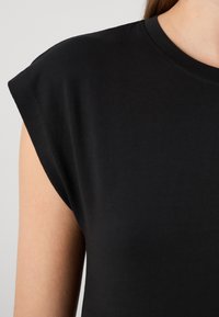 Camiseta negra de manga corta hecha de una tela suave, con un cuello redondo y un diseño de hombros ligeramente acolchado.