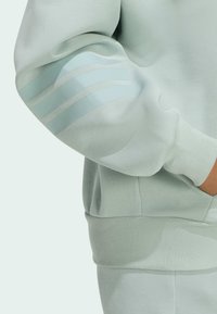 Mentolový svetr s ribbovaným manžetem a lemem, se třemi reflexními pruhy na lokti pro zvýšení viditelnosti a detaily.