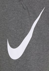 El tejido de la sudadera gris presenta un gran y prominente logo de swoosh en blanco de Nike. La textura parece suave y casual, con un diseño sencillo.