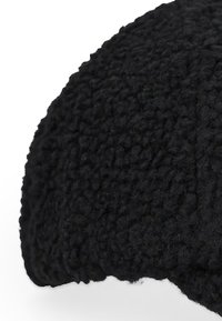 Cappello di fleece nero con una superficie texture, caratterizzato da un design arrotondato e un materiale morbido e soffice. Il bordo è leggermente arricciato.