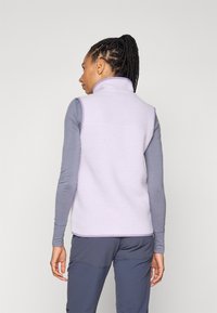 Gai purpura vilnas veste ar augstu apkakli, tekstūra atgādina mīkstu šērlingu. Valkāta pār garām piedurknēm pelēku krekli, bez redzamām aizdaremi.