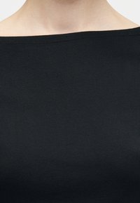 Κοντινή λήψη ενός ατόμου που φοράει μαύρο ριμπ τοπ με έξω τους ώμους, δείχνοντας το ντεκολτέ και την περιοχή του άνω στήθους.