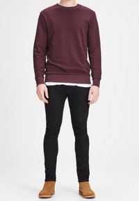 Bordeauxrode crewneck trui met geribbelde manchetten, gecombineerd met zwarte slim-fit jeans en lichtbruine enkellaarzen. Eenvoudig ontwerp, geen patronen of prints.