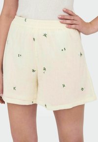 Pantalones cortos bordados de color amarillo claro, hechos de una tela texturizada con diseños florales verdes, que cuentan con una cintura elástica y un corte relajado.
