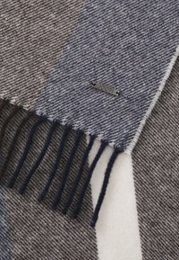 Wollen sjaal met een houndstooth patroon in grijs en marineblauw, met franjes aan de randen en een klein metalen logo label.