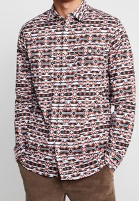 Lang shirt met lange mouwen en geometrische patronen in zwart, wit en roestkleuren, gemaakt van lichtgewicht stof met een knoopsluiting aan de voorkant.