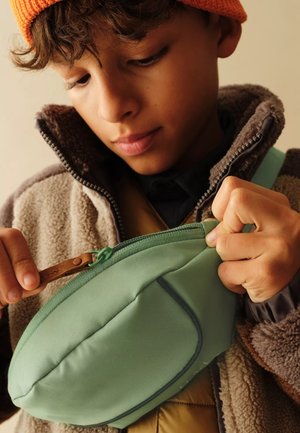 Grüner Stoffbeutel mit einer geschwungenen Form, Reißverschluss und Lederziehfleck, eingebettet in eine weiche Fleecejacke.