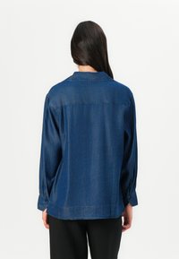 Denimskjorta i mörkblått, med krage, långa ärmar med knappmanchetter och en avslappnad passform. Slät textur med subtil glans.