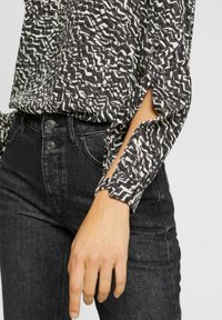 Blusa a righe in bianco e nero con spacco laterale, abbinata a jeans in denim nero a vita alta con dettagli in bottone. Tessuto testurizzato.