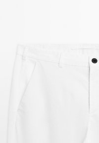 Weiße Baumwollhosen mit flacher Vorderseite, zwei seitlichen Taschen, einem schwarzen Knopfverschluss und Gürtelschlaufen. Glatte Textur mit einem klaren Finish.