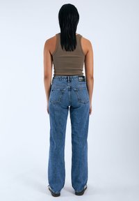 Top in maglia a coste marrone, jeans blu a vita alta con gamba dritta, due tasche posteriori e etichetta nera in vita.