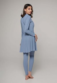 Lichtblauwe, langmouw tuniekjurk met een uitlopende zoom, gecombineerd met bijpassende leggings. Gemaakt van een gladde, elastische stof.