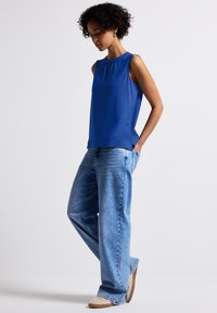Top senza maniche blu realizzato in tessuto morbido, abbinato a jeans a gamba larga di un blu chiaro. L'outfit presenta una vestibilità comoda e un design minimalista.