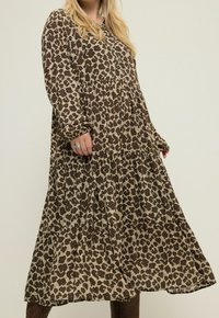 Robe à manches longues à imprimé léopard marron et beige, taille froncée, silhouette fluide, avec des détails subtils de boutons. Texture de tissu douce.