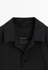 Zwarte buitenkleding met een reverskraag en een enkele knoop. Heeft een gladde textuur en een label met de tekst "Massimo Dutti."