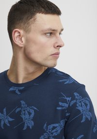 Marineblå hettegenser med blomsterdesign i lys blå. Rund halsdesign med en glatt tekstur og lett stoff.