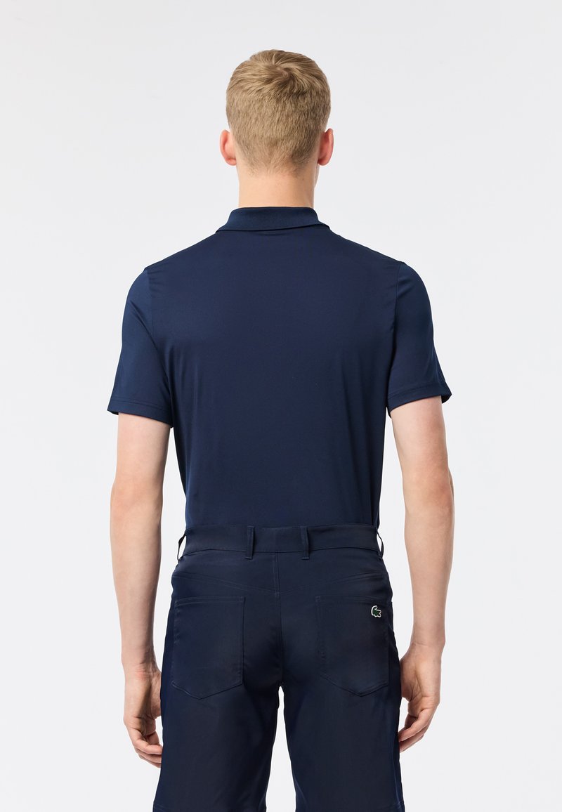 Polo shirt navy a maniche corte con colletto, tessuto liscio, e un piccolo logo sulla schiena, abbinato a pantaloni scuri coordinati.