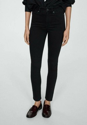 Jeans ajustados negros de mezclilla, con una cintura alta, diseño clásico de cinco bolsillos y detalles de costura sutiles. Combinados con mocasines oscuros.