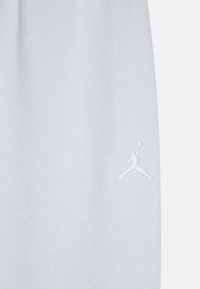 Svetlomodrá tkanina z bavlny, ktorá je zmesou, s bielou vyšitou značkou Jumpman na dolnej ľavej strane. Mäkka textúra, neformálny dizajn.
