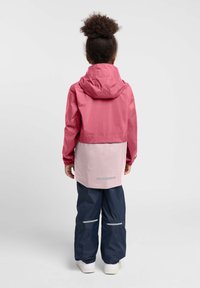 Rosa und hellrosa wasserdichte Jacke mit Kapuze, ausgestattet mit elastischen Bündchen. Kombiniert mit navyblauen wasserdichten Hosen mit reflektierenden Akzenten.