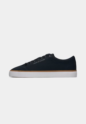 Black low-top sneaker with white sole, brown trim, and "Tommy Hilfiger" logo on side, displayed on plain light background.