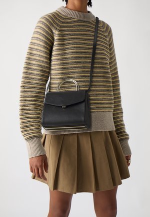 Bolso de cuero negro con asa superior y herrajes dorados, combinado con un suéter de punto a rayas en tonos beige, oliva y gris, y una falda plisada.
