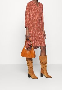 Vestido color óxido con estampado floral blanco, cintura entallada y escote en V. Bolso de cuero marrón y botas de ante hasta la rodilla.