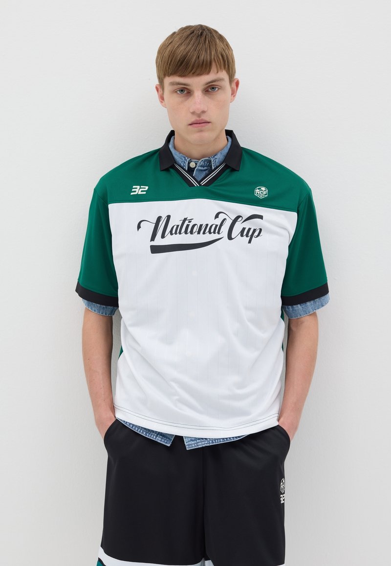 Maillot de sport vert et blanc avec le texte "Coupe nationale", accents noirs, manches courtes et un col, associé à un short noir.